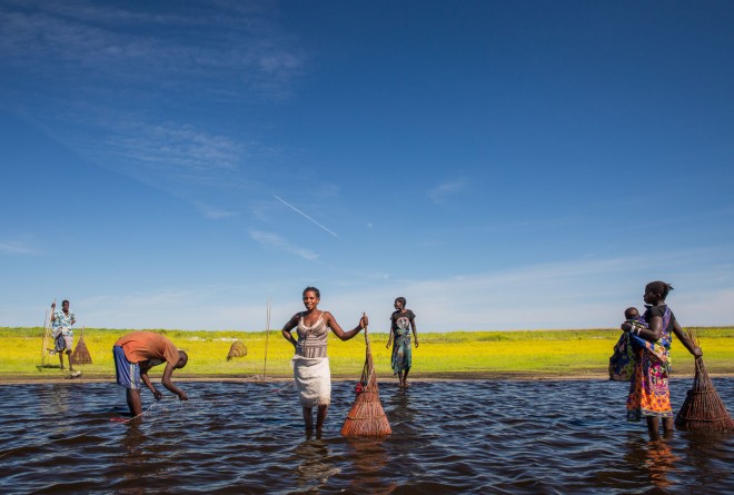 Men and women checking nets in the water under a deep blue sky